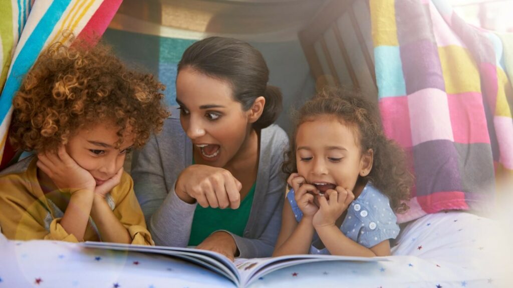 A woman and two kids reading a book together inside an indoor tent.