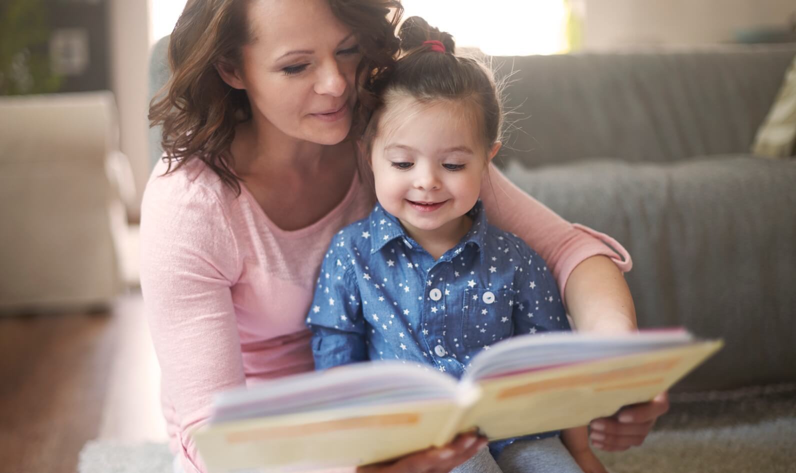 An adult and child sitting on the floor reading a book